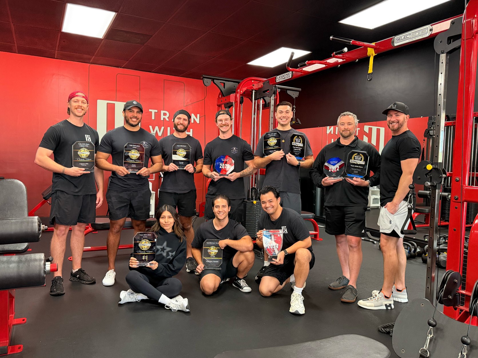 The full Train With Dave coaching team holding their Best of Orange County personal training awards inside the studio